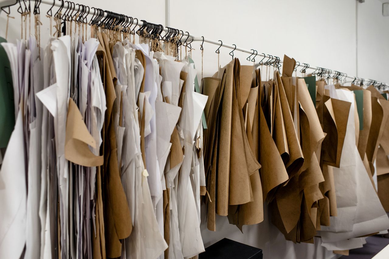 Rack with various paper sewing patterns for dress making on hangers placed near white wall inside fashion apparel designer workshop